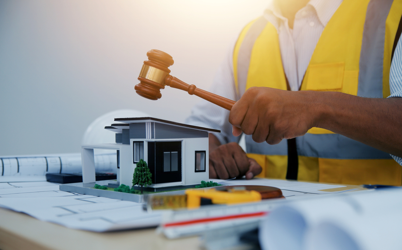 Construction worker holding judge's gavel above 3D home blueprints